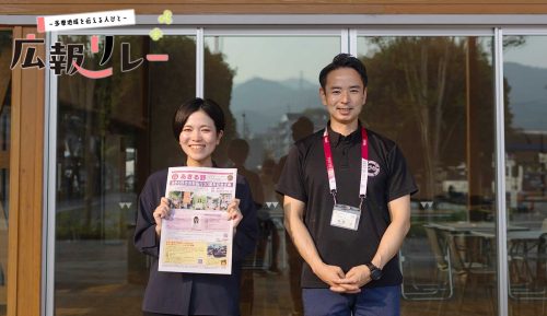 インタビューを行ったフレア五日市の前に立つあきる野市広報担当の豊島さん(左)と茅根さん(右)。豊島さんはあきる野市の広報紙を持っている。(左上に多摩地域を伝える人びと 広報リレー のロゴ入り)