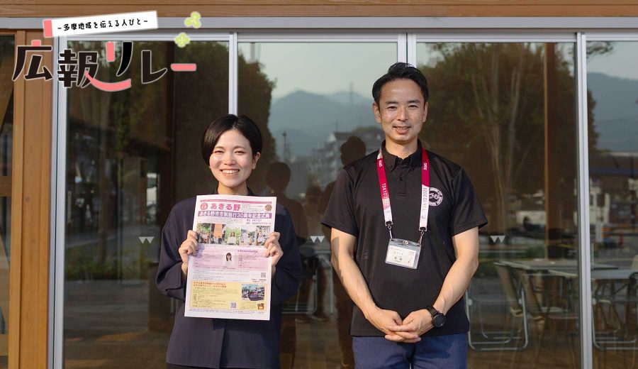インタビューを行ったフレア五日市の前に立つあきる野市広報担当の豊島さん（左）と茅根さん（右）。豊島さんはあきる野市の広報紙を持っている。（左上に多摩地域を伝える人びと 広報リレー のロゴ入り）