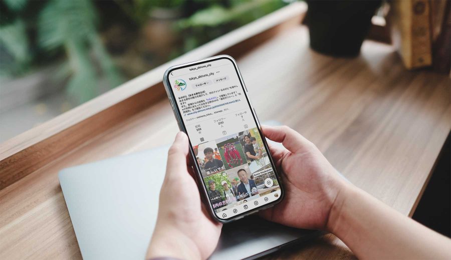 デスクに向かい、スマートフォンであきる野市の公式インスタグラム「るのびと」を閲覧している手元